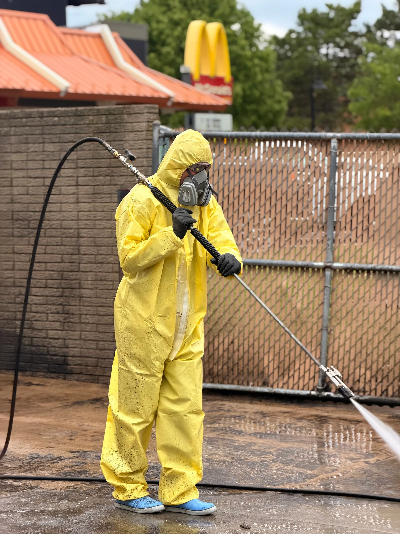 MPWS technician in a full protective suit and respirator pressure washing a fast-food restaurant pad