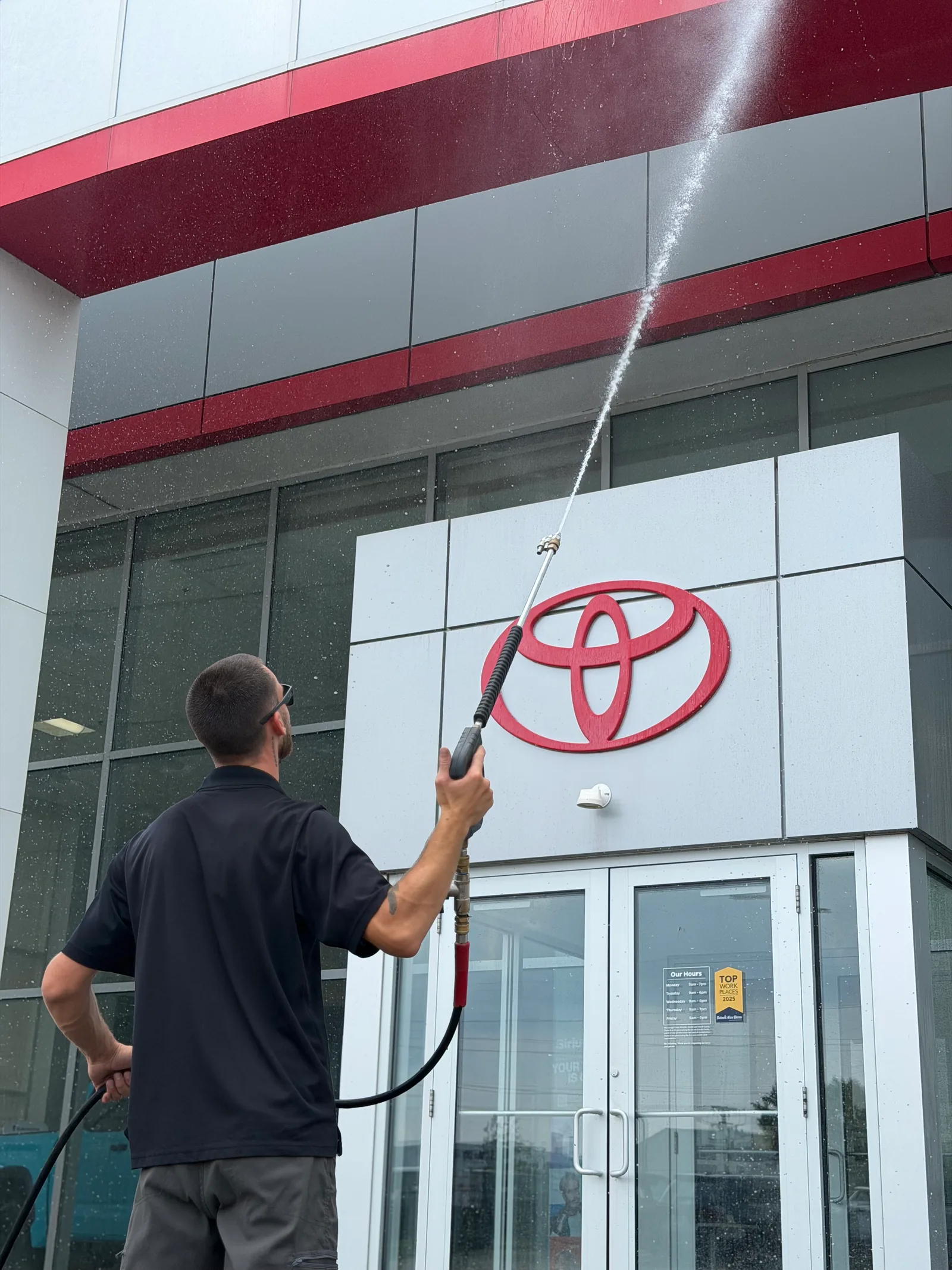 MPWS technician rinsing the glass entry and signage of a Toyota dealership