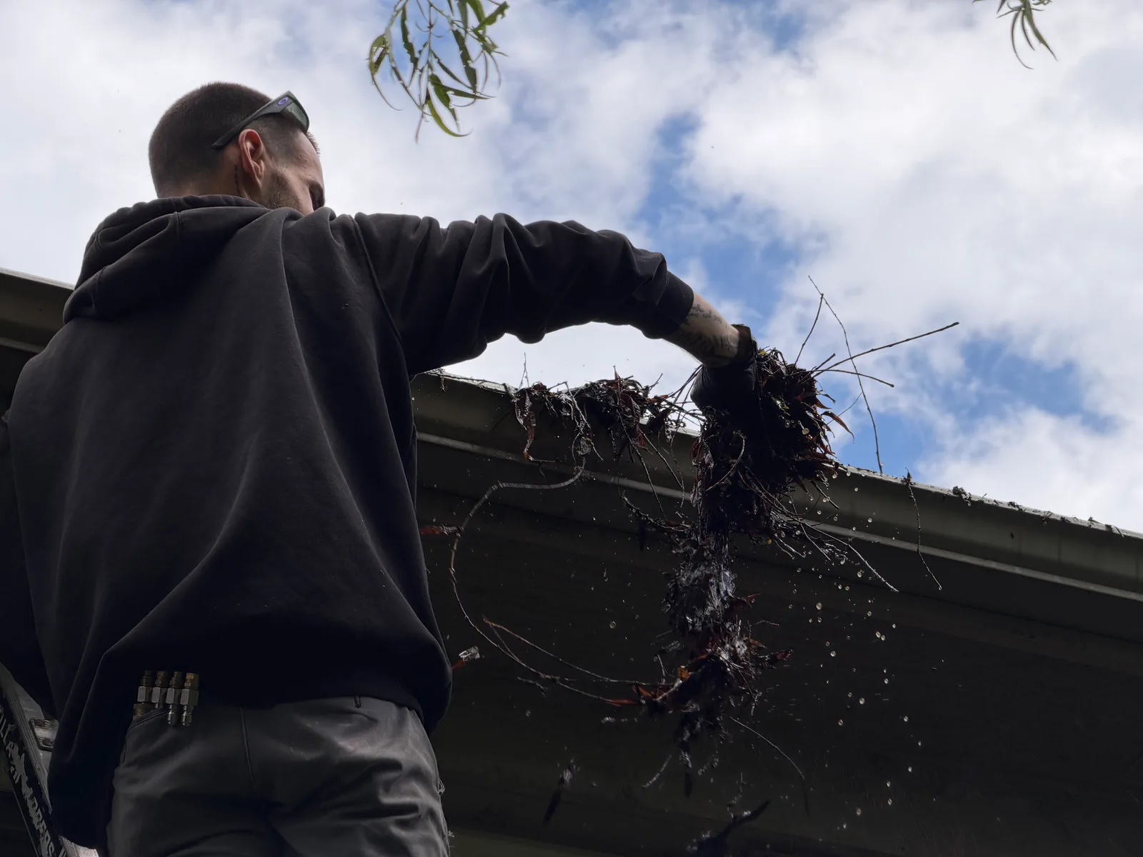 MPWS technician pulling a handful of packed wet leaves out of a gutter